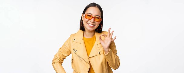 Excellent. Smiling asian girl shows okay, ok sign, nod in approval, recommending smth good, standing over white background - Photo, Image