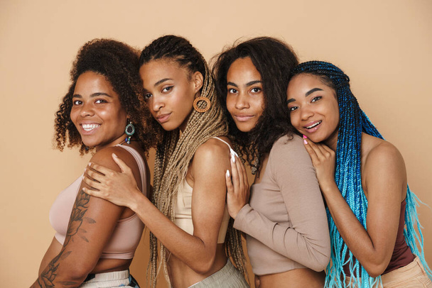Young black four women hugging and smiling at camera isolated over beige background - Fotoğraf, Görsel