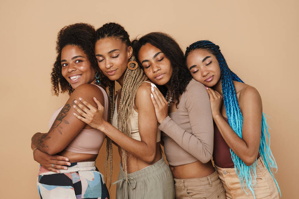 Young black four women hugging and smiling at camera isolated over beige background - Foto, immagini