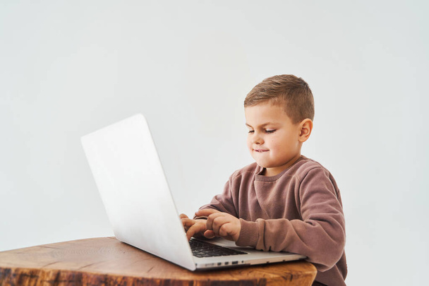 Knappe jongen gebruikt laptop en kijk naar de camera, bekijk virtuele lezing en tutorial. E-learning en kennis. Voorbereiding van de les en online studeren op witte achtergrond - Foto, afbeelding