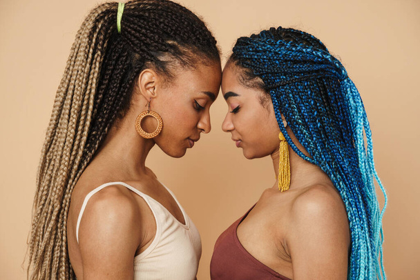 Young black two women with afro pigtails posing with head to head isolated over beige background - Foto, immagini