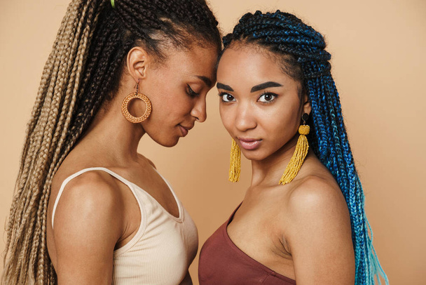 Young black two women with afro pigtails posing with head to head isolated over beige background - Foto, Imagem