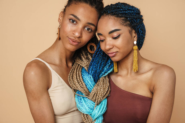 Joven negro dos mujeres abrazándose mientras posan en cámara aislada sobre fondo beige - Foto, imagen