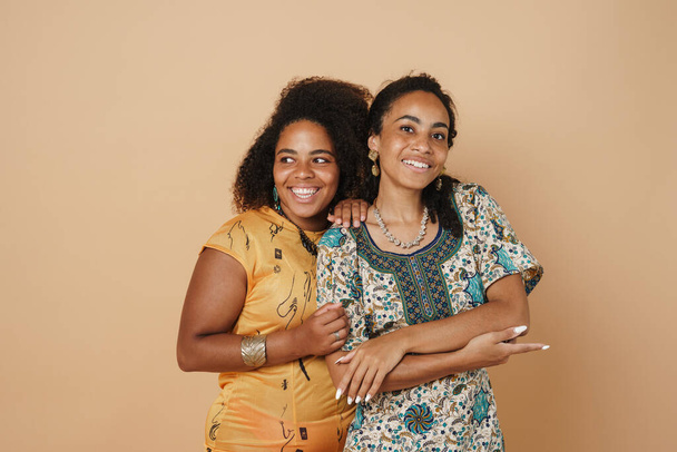 Young black two women hugging and laughing at camera isolated over beige background - Foto, imagen