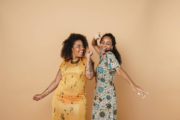 Young black two women dancing and laughing at camera isolated over beige background - Photo, Image