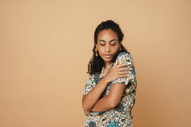 Young black woman wearing dress posing on camera isolated over beige background - Foto, afbeelding