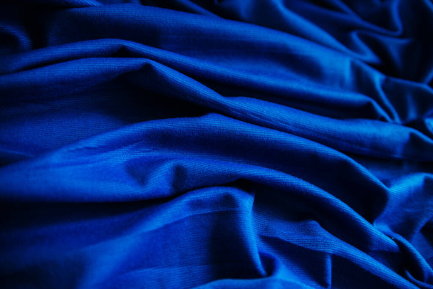 Tejido envuelto en arrugas azules. El material de coser está sobre la mesa. Textura de costura con pliegues - Foto, Imagen