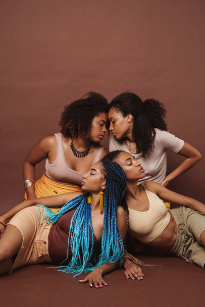 młody czarny cztery kobiety pozowanie razem na kamery odizolowane na brązowy tło - Zdjęcie, obraz