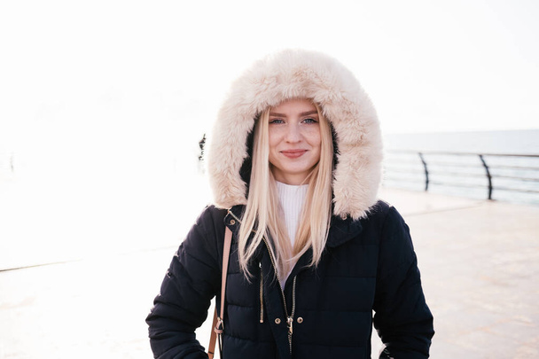 Happy smiling blonde girl in a fluffy hood on a white background. Portrait. - Foto, Imagem