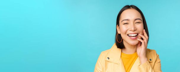 Nahaufnahme Porträt eines natürlichen asiatischen Mädchens lachend, lächelnd und glücklich aussehend, vor blauem Hintergrund stehend - Foto, Bild