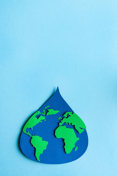 Water drop cut out on paper with world map on light blue background. Copy space. Vertical photo. Top view. - Foto, afbeelding