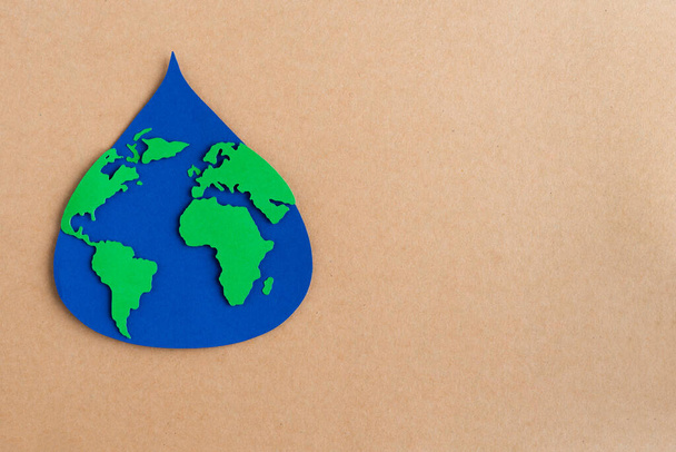 Goccia d'acqua ritagliata su carta blu con mappa del mondo su sfondo cartoncino marrone. Copia spazio. - Foto, immagini