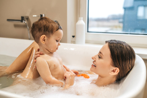 Smiling woman taking a bath with her baby - Фото, зображення