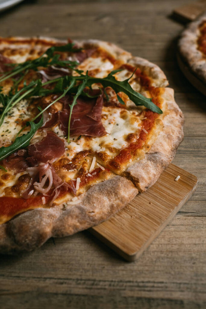 Heerlijke warme vleespizza met prosciutto en salami op een houten tafel. - Foto, afbeelding