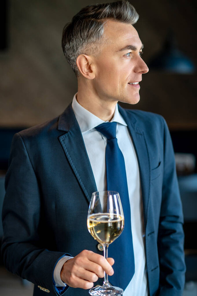 An elegant man in a suit with a glass of wine in hands - Fotoğraf, Görsel