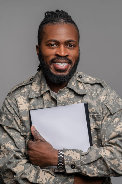 Усміхнений молодий солдат тримає документи в руках
 - Фото, зображення