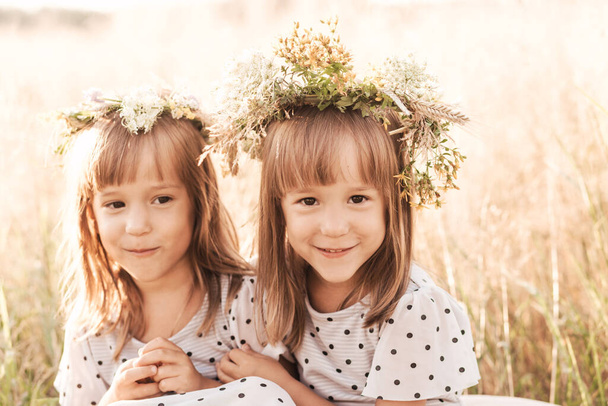 Δύο μικρά ευτυχισμένα δίδυμα κορίτσια που παίζουν μαζί στη φύση το καλοκαίρι. Γυναικεία ιδέα φιλίας και νεότητας. Τρόπος ζωής των ενεργών παιδιών. - Φωτογραφία, εικόνα
