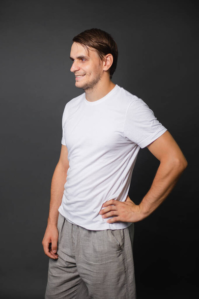 A handsome young man in a white t-shirt stands on a gray background. Clothes for the inscription. mockup - Photo, image