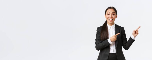 Izgalmas női ázsiai menedzser, értékesítő vagy ingatlanügynök bemutató ház eladó, ujjal mutogatva jobbra, kereskedő be projekt vagy chart üzleti találkozón, álló öltöny fehér háttér - Fotó, kép