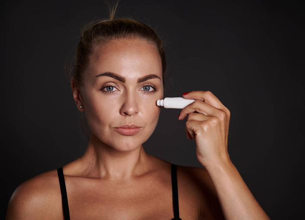 Beautiful middle aged woman applying anti puffiness anti wrinkles moisturizer under eyes. Youth concept and prevention of first signs of aging process. - Foto, Imagem