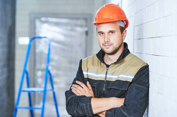 Construction worker standing indoors in uniform and helmet. Concept of building contractor or service employee - Valokuva, kuva