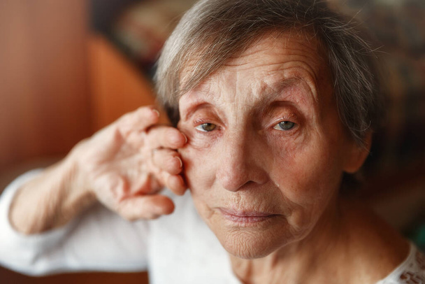 Senior mulher solitária sentado em casa e olhando para a câmera. Velha mulher está chorando e enxugando lágrimas - Foto, Imagem