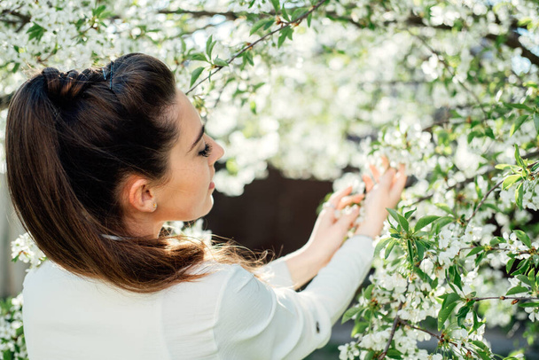 Spring is coming. Natural beauty. Beautiful young woman among white blossoms in spring garden. Young woman enjoying scent in blooming spring garden - Фото, изображение