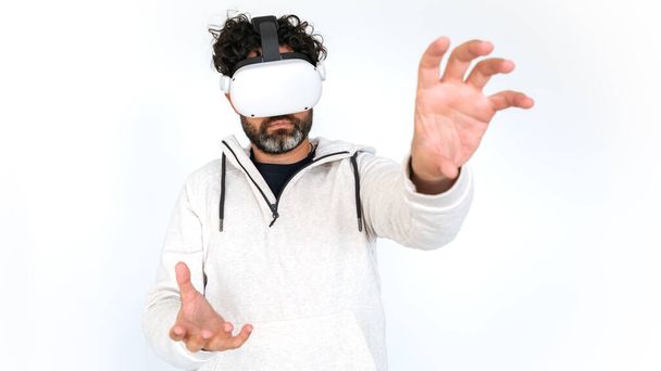 Bearded man watching movie with VR glasses headset on white background. Play video game simulator enjoy immersive futuristic virtual reality 3D - Photo, image