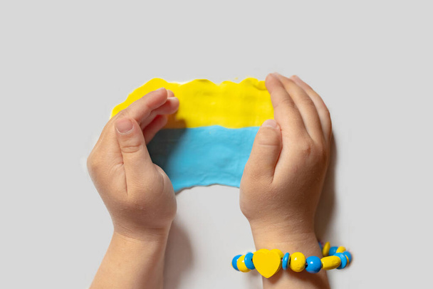 Un enfant faire le drapeau de l'Ukraine pâte. Enfant avec de la plasticine dans les couleurs du drapeau de l'Ukraine dans les mains. La créativité des enfants. bricolage artisanat de vacances et des outils d'artisanat. Priez pour l'Ukraine. - Photo, image