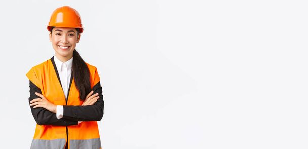 Hymyilevä itsevarma aasialainen naisjohtaja rakennuksessa, rakennustyöntekijä turvakypärä ristissä ja näyttää päättäväiseltä. Assertive arkkitehti esitellä hankkeensa sijoittajille - Valokuva, kuva