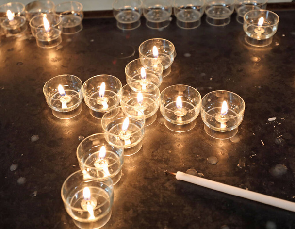 зажженные свечи с пламенем, которые образуют крест в христианской церкви во время мессы - Фото, изображение