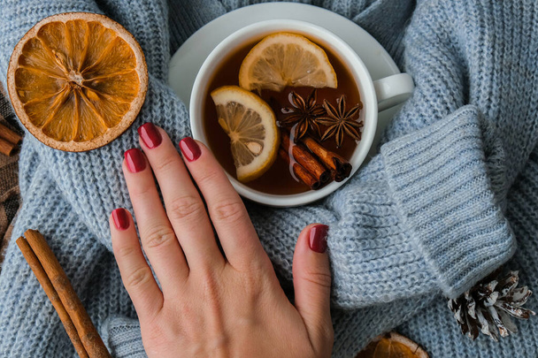Blue sweater and cup of hot tea with lemon cinnamon sticks and anise star. Dry slices of citrus orange and cones. Hot winter cocktail. Christmas, Thanksgiving drinks. Autumn, grog, hot sangria, mulled wine. Festive holiday flat lay atmosphere - Foto, Imagen