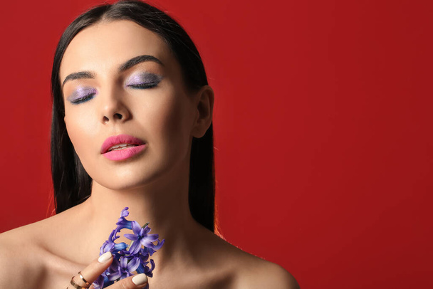 Krásná mladá žena s tvůrčí make-up a hyacint květiny na červeném pozadí - Fotografie, Obrázek