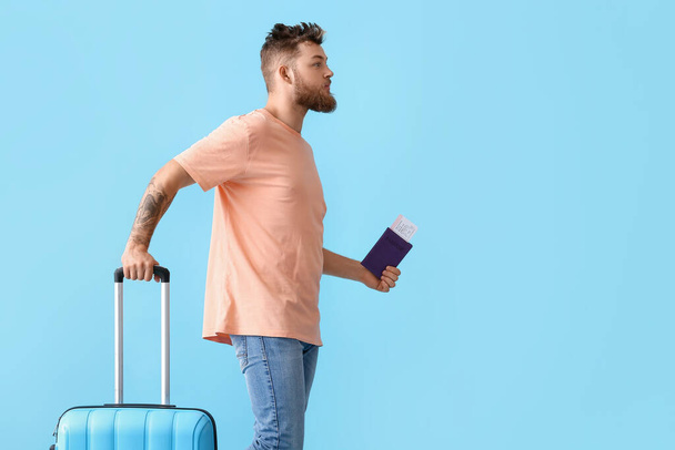 Przystojny mężczyzna z paszportem i walizką na niebieskim tle - Zdjęcie, obraz
