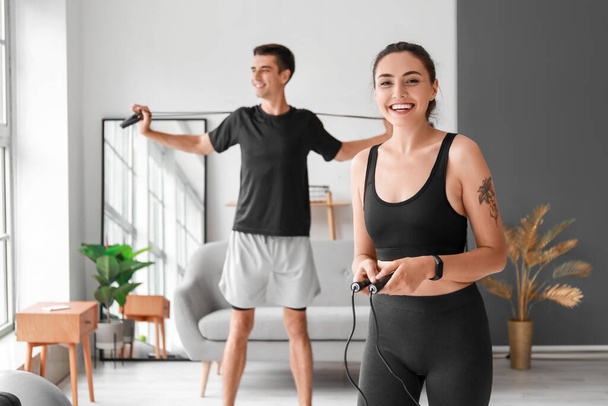 Sporty young couple jumping rope at home - Zdjęcie, obraz