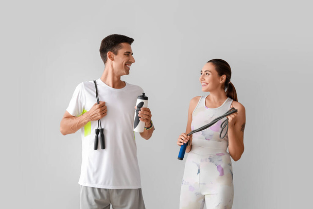 Sportliches junges Paar mit Springseilen auf grauem Hintergrund - Foto, Bild