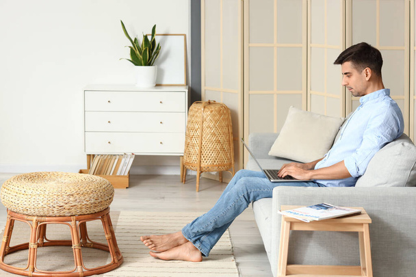 Joven hombre descalzo utilizando el ordenador portátil en el sofá en casa - Foto, imagen