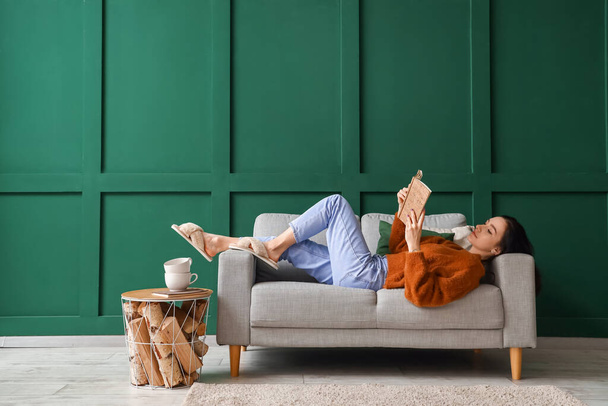 Красивая молодая женщина с книгой отдыхает на диване дома - Фото, изображение