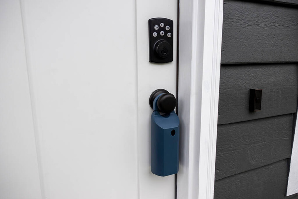 View of a white door with keypad entry and a real estate lock box around the door knob - Photo, Image