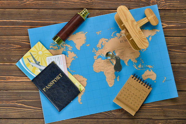 Passport with spyglass, airplane, calendar and world map on dark wooden background - Photo, image