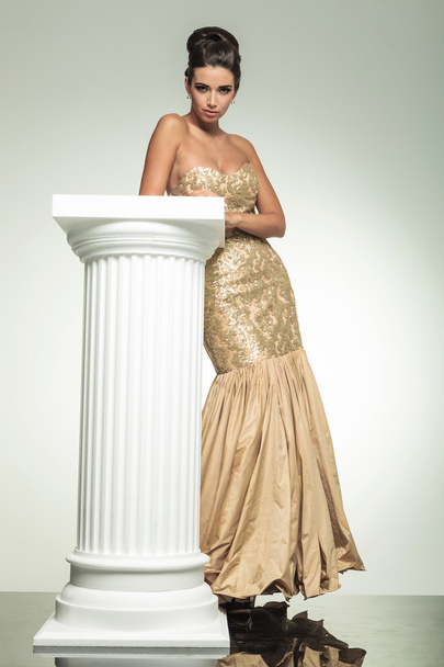 модна елегантна жінка в золотій сукні, що спирається на колону
 - Фото, зображення