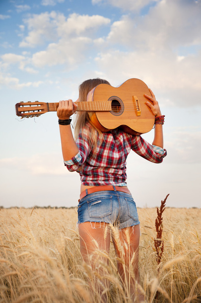 Beautiful girl with a guitar on a background of a wheat field, view from the back - Photo, image
