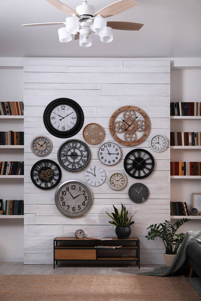 Stylish room interior with console table, beautiful houseplants and collection of different clocks on white wall - Foto, Imagem