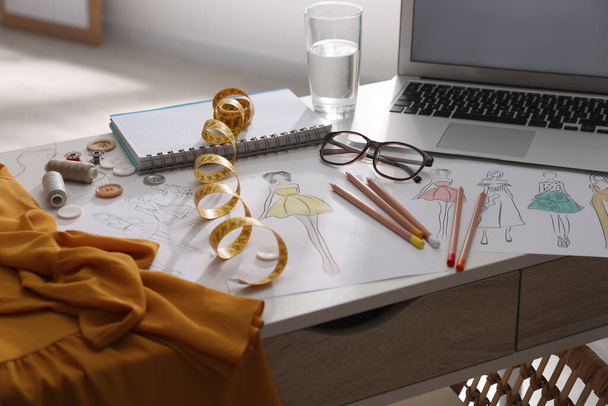 Sketches of clothes and different stuff on white table indoors. Fashion designer's workplace - Photo, image