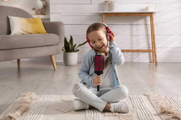 Cute little girl in headphones with hairbrush singing at home - Fotoğraf, Görsel