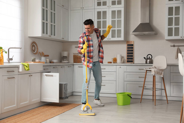 Man with mop singing while cleaning at home - Foto, afbeelding
