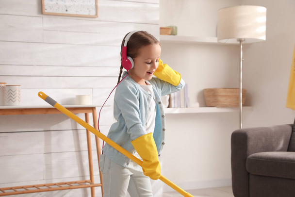 Cute little girl in headphones with mop singing while cleaning at home - Foto, Bild