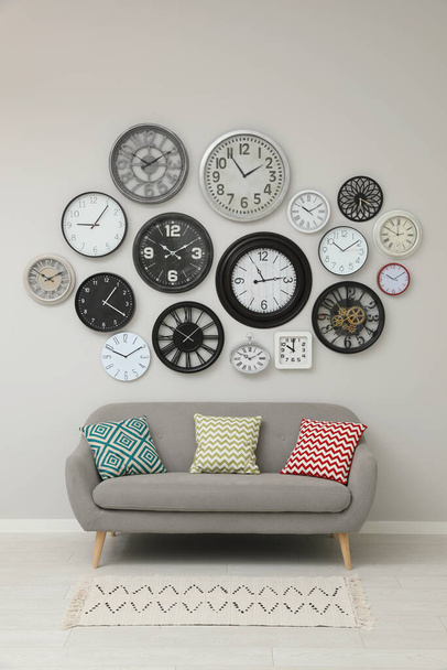 Sofa and many different clocks hanging on white wall in room - Foto, Imagen