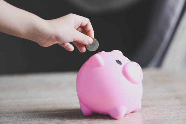 Child hand putting money coin into piggy bank for saving money for education study, Save money concept - Photo, Image