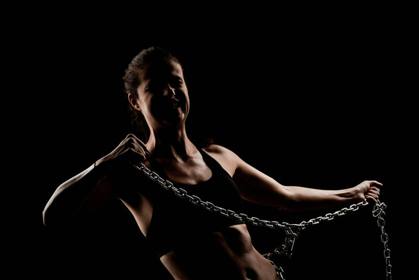 Strong fit girl with metal chain. Pulling and posing against black background - 写真・画像